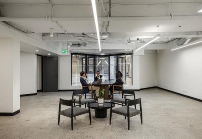 Meeting area with a round table and grey chairs under linear LED lighting.
