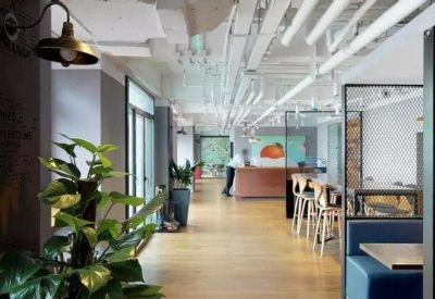 Long bright corridor with hanging plants, wooden floors, and a blue booth seating area.