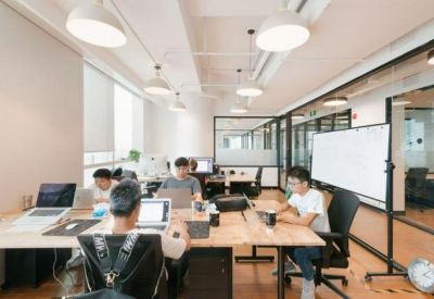 Open-plan workspace with individuals working at wooden desks under modern pendant lighting.