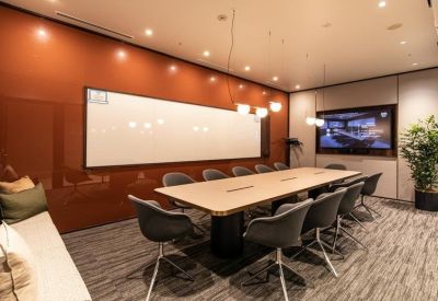 Boardroom with a long light-wood table, grey chairs, and a large whiteboard on a terracotta wall.