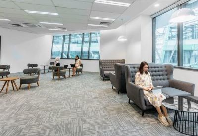Spacious communal lounge area with plush grey armchairs and high ceilings.