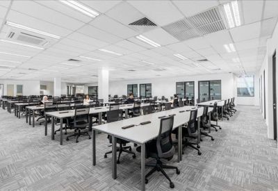 Large open-plan office space featuring long white desks and ergonomic mesh chairs.