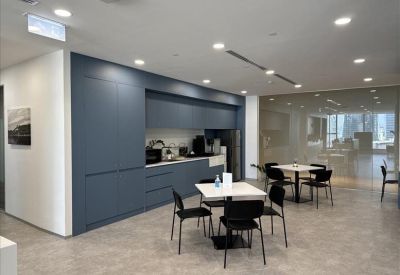 Modern communal kitchen and dining area with blue cabinetry and white tables.