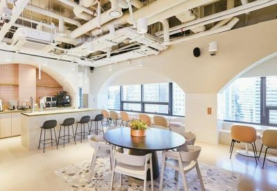 Spacious communal lounge with exposed ceiling pipes, round tables, and a breakfast bar.