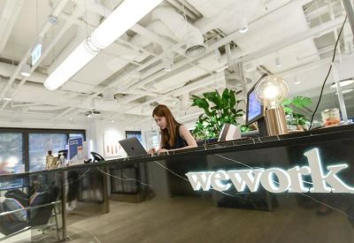 Branded reception desk area with a receptionist, indoor plants, and exposed ceiling.