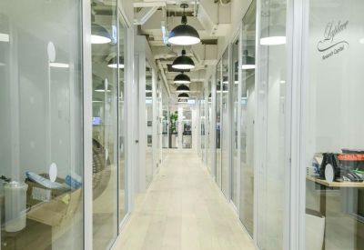 A hallway lined with glass-walled private office suites under industrial-style lighting.
