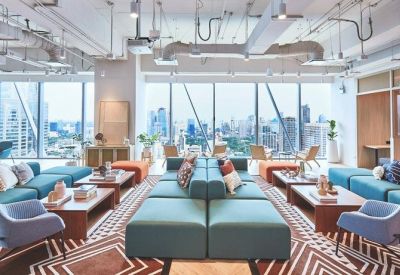 Bright communal lounge with teal sofas, wooden coffee tables, and panoramic city views.