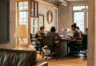 Team collaboration space with people working at a large wooden desk in a bright office.