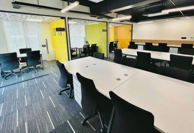 Shared office space with long white desks, black chairs, and yellow accent walls.