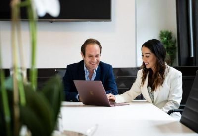 Two colleagues collaborating over a laptop in a bright, modern office setting.