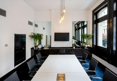 Bright boardroom featuring a long white table, black chairs, and large windows.