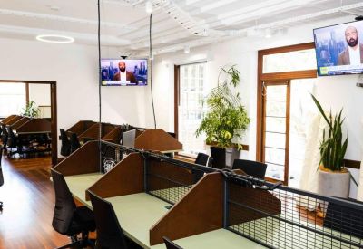 Bright open-plan workspace featuring rows of desks with privacy dividers and wood flooring.