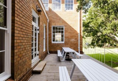 Exterior brick courtyard featuring white picnic benches and large leafy trees.