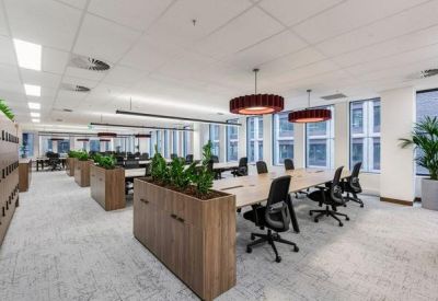 Open-plan workspace with multiple rows of desks, ergonomic chairs, and large windows.