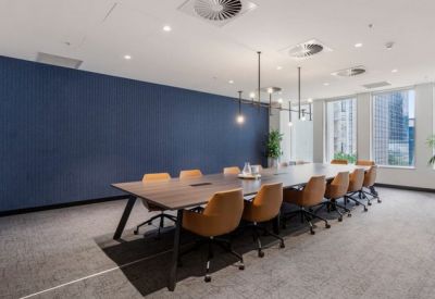 Professional boardroom with a long wooden table, tan leather chairs, and a blue feature wall.