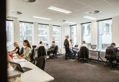 Open-plan workspace with employees working at white desks near large windows.