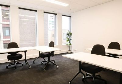 Bright office space with white desks, black chairs, and a potted plant.