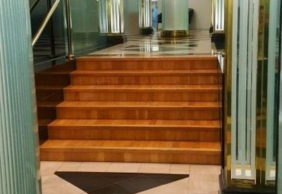 Polished wooden staircase leading to a brightly lit lobby with marble flooring.
