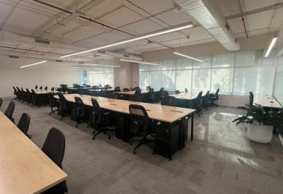 Open-plan office space with rows of long desks, ergonomic chairs, and industrial-style ceiling lights.