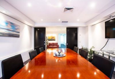 Spacious boardroom with a polished wood table, black leather chairs, and a flat-screen TV.