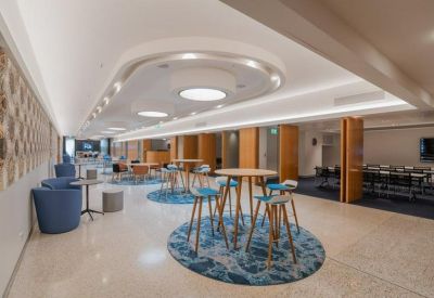 Bright breakout area with high tables, blue stools, and circular light fixtures.