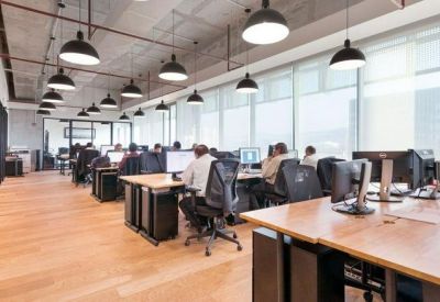 Open-plan office space with rows of desks, black swivel chairs, and large windows.