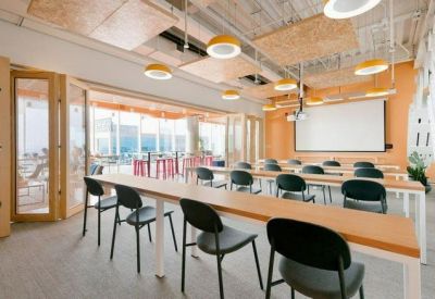 Sunny training room with rows of tables, black chairs, and a presentation screen.