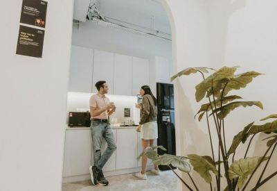 Bright office kitchen area with two people talking and a large leafy plant.