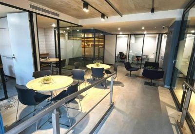 Spacious coworking area with round tables and glass-walled private offices.