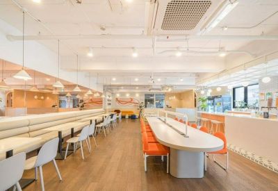 Bright open-plan workspace featuring a long oval communal table and orange seating.