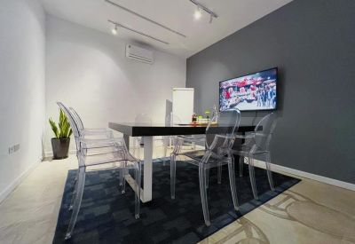 Small meeting room with transparent chairs, a dark rug, and a wall-mounted monitor.
