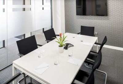 Bright four-person meeting room with a white table and black chairs behind a glass partition.