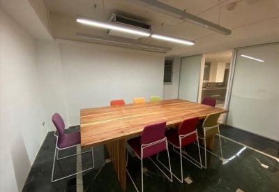 Meeting room featuring a long wooden table and colorful chairs under bright strip lighting.