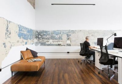 Modern workspace with a tan leather chaise lounge and a rustic distressed feature wall.