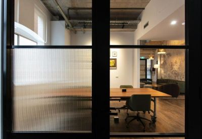 Meeting room viewed through a glass partition featuring a long wooden table and ergonomic chairs.