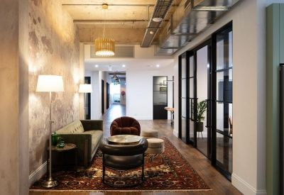 Bright breakout area with a green sofa, floor lamp, and exposed ceiling pipes.