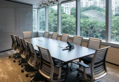 Bright conference room with a long dark table, grey chairs, and a large window overlooking trees.
