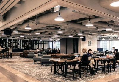Large open-plan coworking space with long wooden tables and various seating areas under industrial ceilings.
