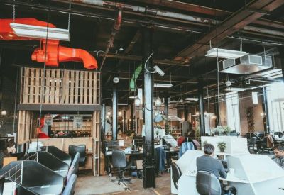 Open-plan office with black workstations and exposed orange ventilation pipes.