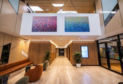 Wide office corridor with light wood floors, brown leather seating, and colorful abstract wall art.