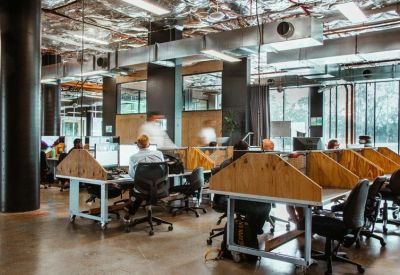 Open-plan coworking area with rows of wooden desks and industrial-style exposed ceilings.