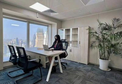 Private office space with a wooden desk, ergonomic chairs, and a large window overlooking the city skyline.