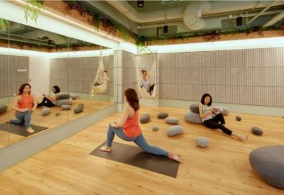 Well-lit wellness studio with wooden floors, mirrors, and people practicing yoga.