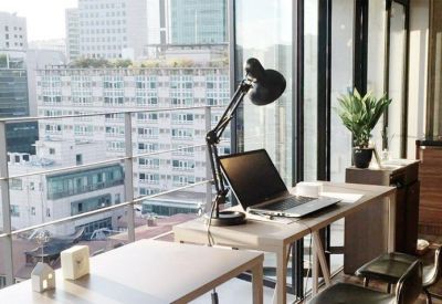 Window-side workstation with a desk lamp and laptop overlooking a dense urban cityscape.