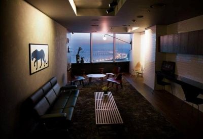 Moody lounge area with a dark leather sofa and a view of the city coastline at dusk.