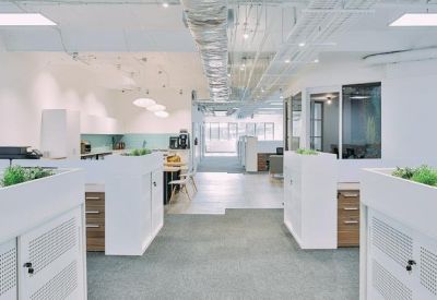 Open-plan office with white workstations, integrated planters, and exposed ceilings.