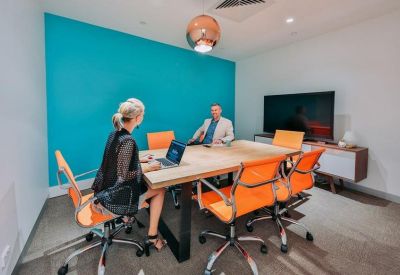 Small meeting room with vibrant orange chairs and a teal feature wall.