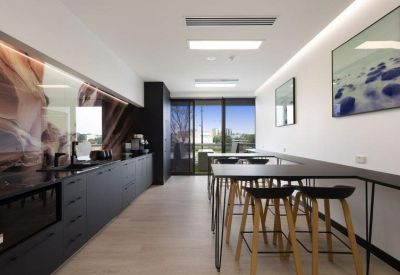 Bright communal kitchen and breakout area with high tables, stools, and vibrant wall art.