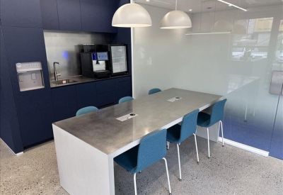 Breakout area with a grey dining table, blue chairs, and a modern kitchenette.