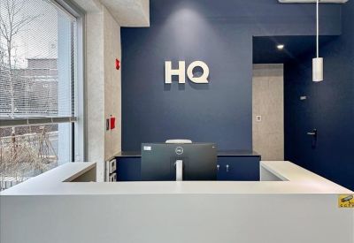 Reception area with a white front desk against a dark blue wall featuring a lit HQ logo.